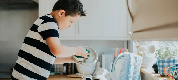 Child in a striped shirt washing dishes at a kitchen sink.