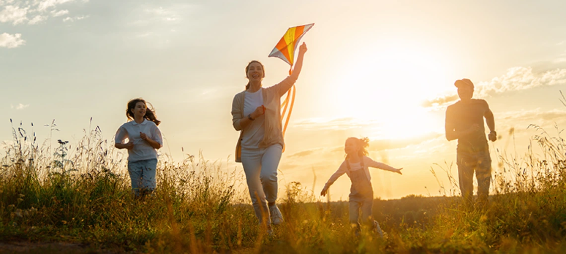 Four people flying colorful kite in sunlit field at golden hour