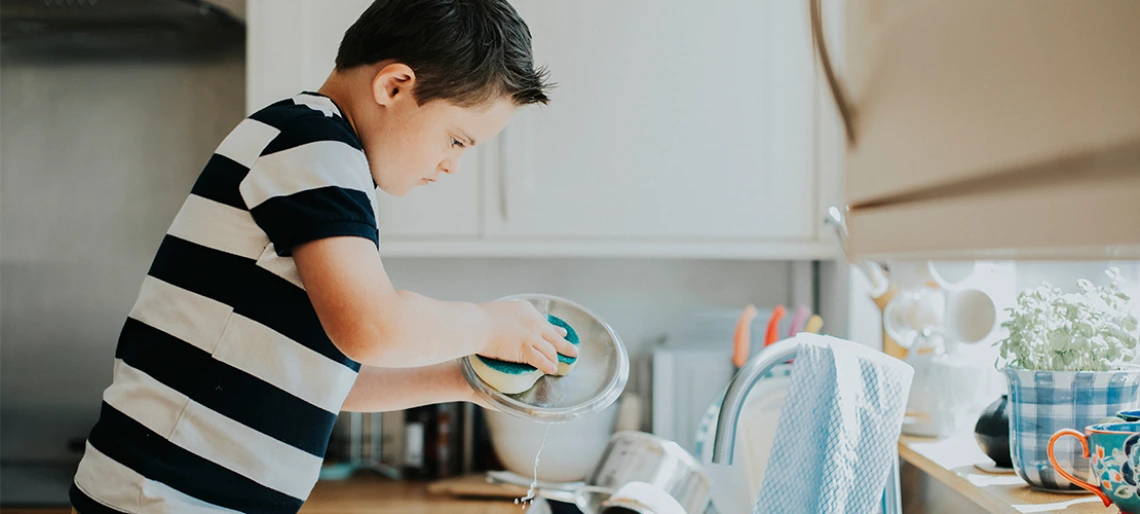 Child in a striped shirt washing dishes at a kitchen sink.